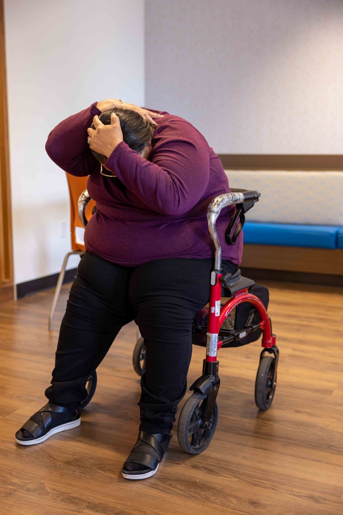 A person sitting in a walking aid covers their head with their hands. The walking aid is in a locked position. (Credit John Falcon)