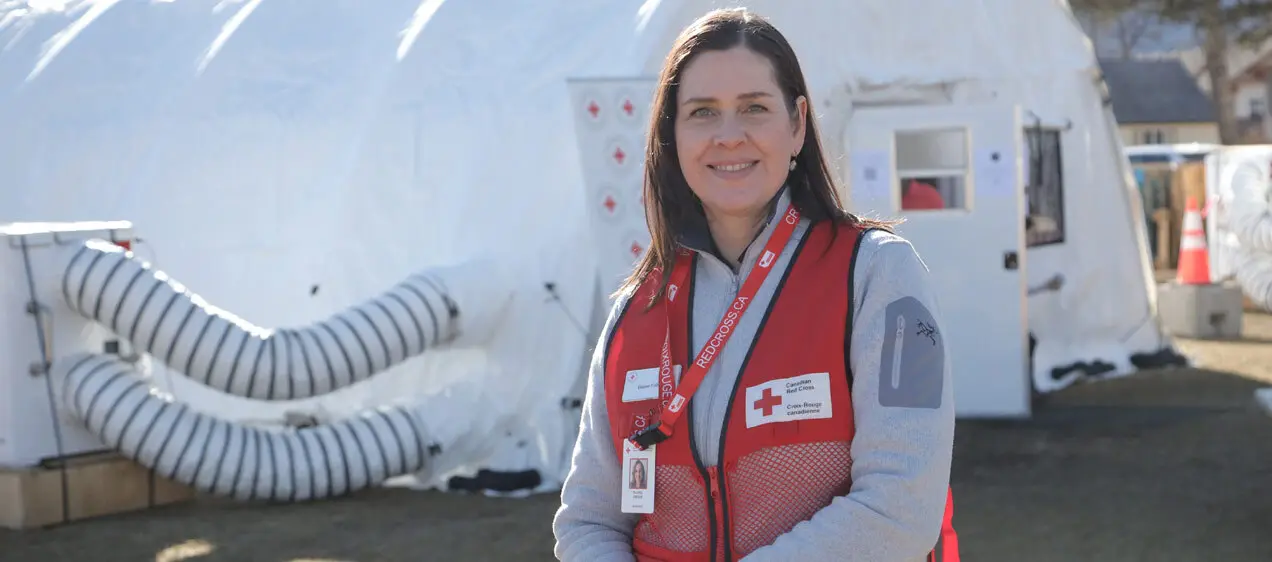 Elaine Fisher, a Red Cross employee, wears a red vest and stands in front of a large pop-up facility in Jasper, Alberta.