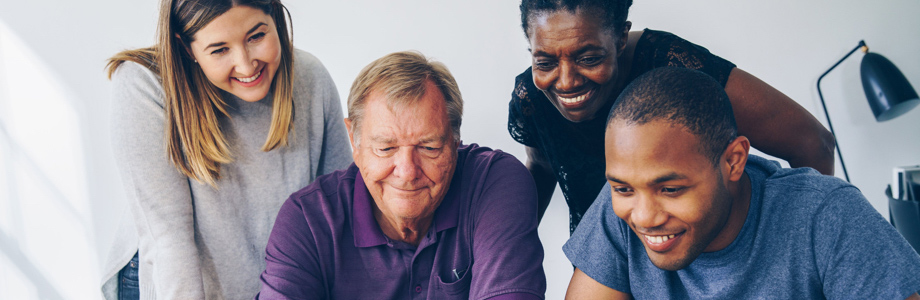 A group of coworkers peer around what appears to be a computer, smiling.