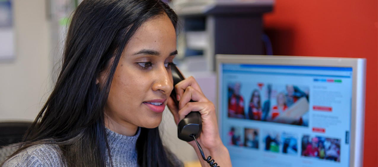 A Red Cross volunteer is on the phone, with a Red Cross webpage visible in the background.