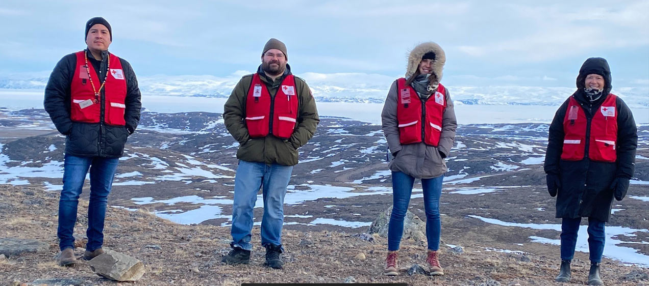 Guy Day Chief, Tim Stringer, Laurence Durocher and Diane Wallace wear red vests and stand atop of a snow covered hill, wearing red vests over their winter coats.