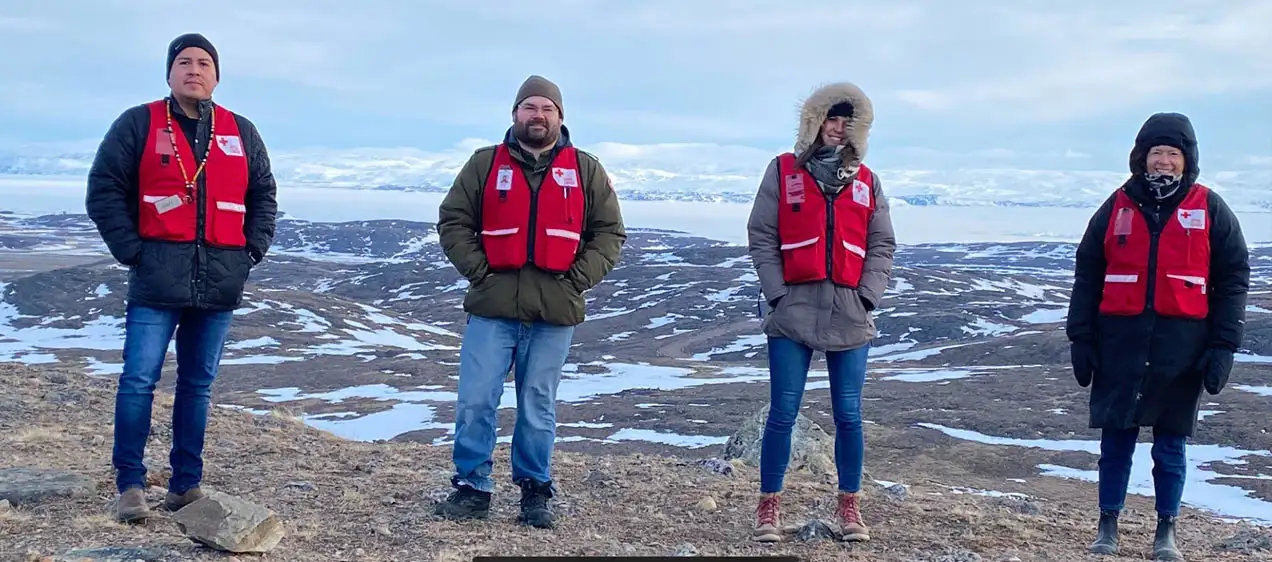Guy Day Chief, Tim Stringer, Laurence Durocher et Diane Wallace portent des gilets rouges et se tiennent au sommet d'une colline couverte de neige, portant des gilets rouges par-dessus leurs manteaux 