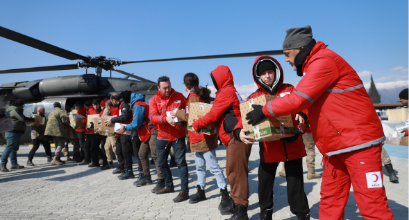 chain of red crescent volunteers unloads supplies from a helicopter