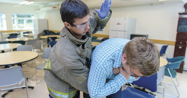 A first responder helps a choking person by placing his arm across their chest and delivering firm back blows while they bend forward.