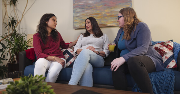 A distressed friend sits on a sofa as her two other friends offer reassurance.