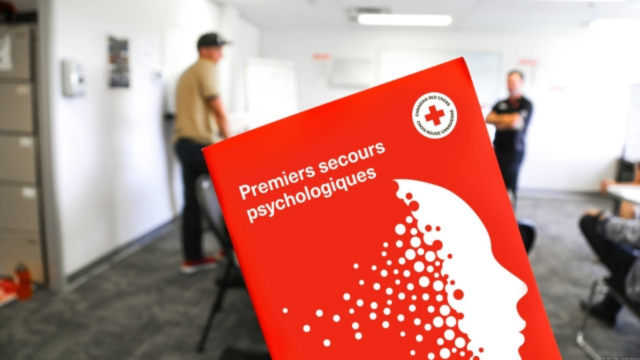 Le livret d’information de la Croix-Rouge canadienne sur les premiers secours psychologiques avec une classe et des personnes en arrière-plan.