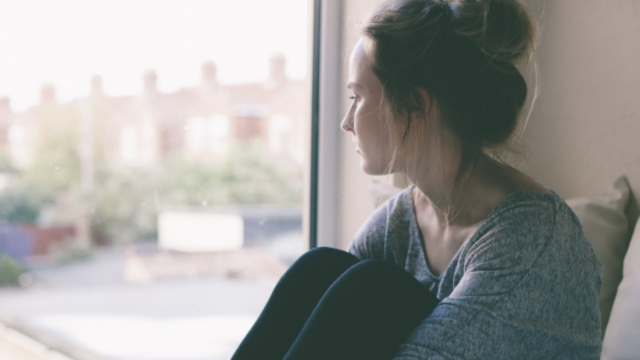 Une personne songeuse regarde par la fenêtre. Elle est assise avec les genoux repliés.