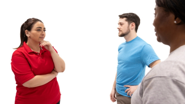 A gathering of friends discussing mental health. One looks curious with arms crossed, while another listens intently. A third stands to the side.