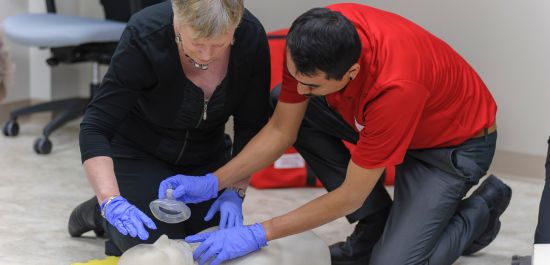 An emergency first aid instructor showing a learner how to place a barrier device over a manikin's mouth and nose to provide rescue breaths.