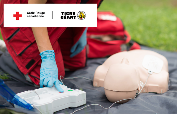 Une monitrice utilise un défibrillateur lors d’une formation en secourisme et RCR. Les logos de la Croix-Rouge canadienne et du Tigre Géant sont affichés dans le bas de l’image.