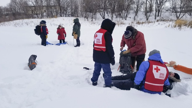 Des personnes portant des dossards de la Croix-Rouge aident une personne souffrant d’une urgence liée au froid en la réchauffant et en lui prodiguant des soins.