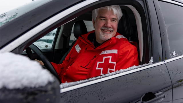 Une personne portant une veste de la Croix-Rouge est assise dans une voiture, soulignant l’importance de la sécurité au volant et d’être prêt à aider autrui en cas d’urgence.