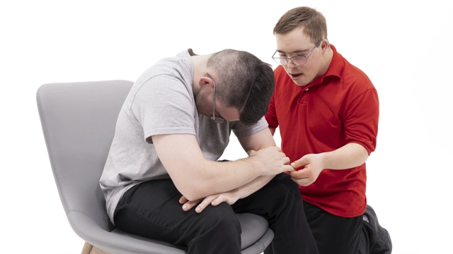 Une personne est assise, la tête baissée, pendant qu’une autre personne l’écoute attentivement et lui offre un soutien émotionnel, ce qui représente les premiers secours psychologiques.