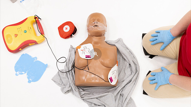 Mannequin de formation à la RCR au sol avec des électrodes de DEA placées sur la poitrine, utilisé pour pratiquer les techniques de défibrillation