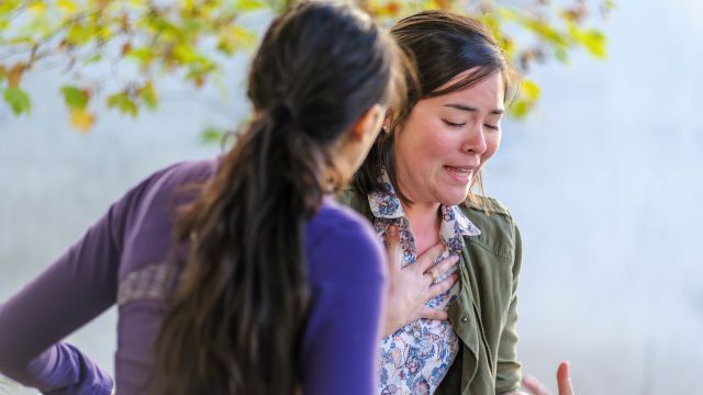 Une personne qui est agitée, se tient poitrine et semble souffrir d’une crise de panique reçoit l’aide d’une autre personne assise avec elle sur un banc de parc.