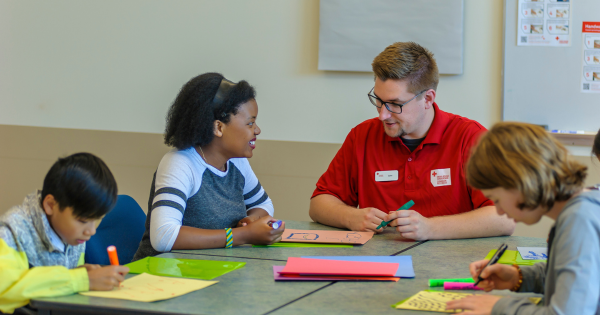 An instructor is doing an orientation with Youth learners. Seated around a table, worksheets and markers are visible.
