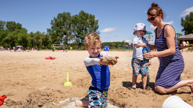 Two children and their parent playing in the sand on the beach on a very sunny day.