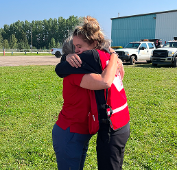 Deux personnes portant des gilets de la Croix‑Rouge canadienne s’enlacent.