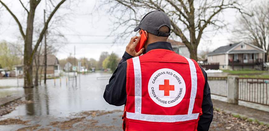 Un homme portant un gilet de la Croix‑Rouge parle au téléphone tout en observant une rue.