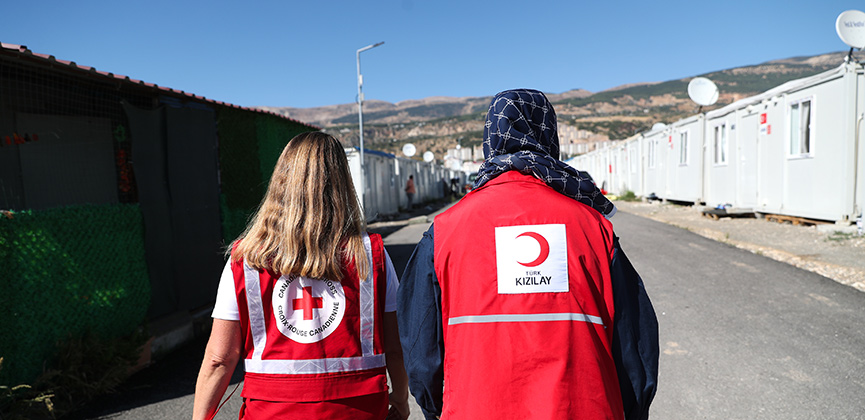 Deux personnes portant des gilets de la Croix-Rouge marchent ensemble.