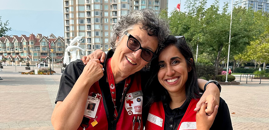 Deux personnes portant des gilets de la Croix‑Rouge sourient et s’enlacent.