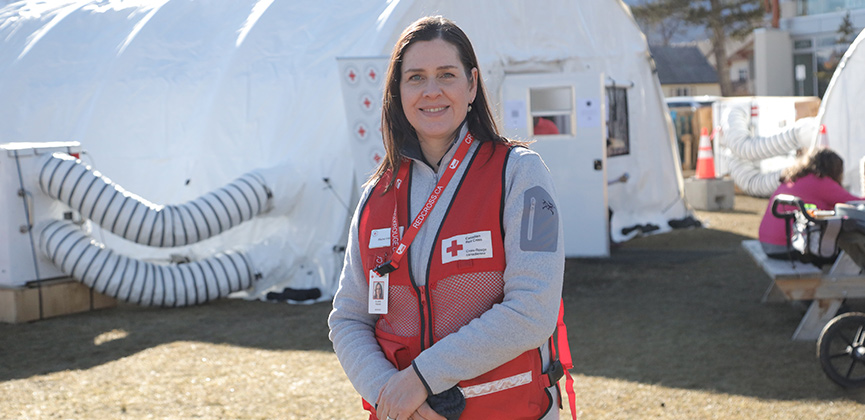 Une femme portant un gilet de la Croix‑Rouge se tient debout, souriante.