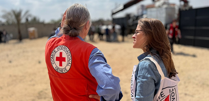 Deux personnes portant des gilets de la Croix‑Rouge regardent vers l’horizon.