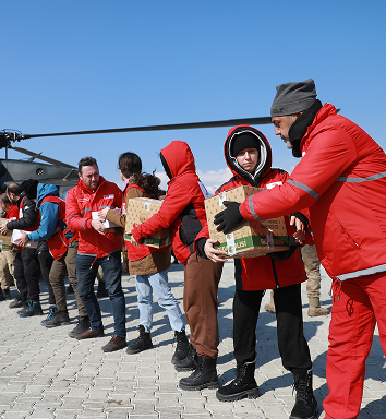 Une file de personnes vêtues de rouge se passent du matériel d’aide d’urgence.