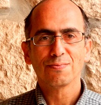 Man with dark hair and glasses in front of stone wall