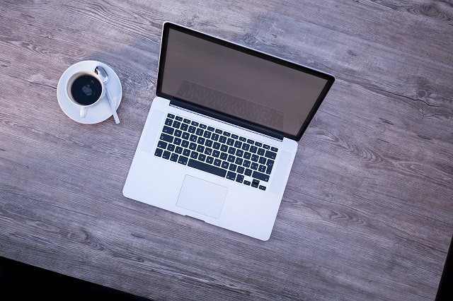 a laptop on a table with a cup of coffee beside it