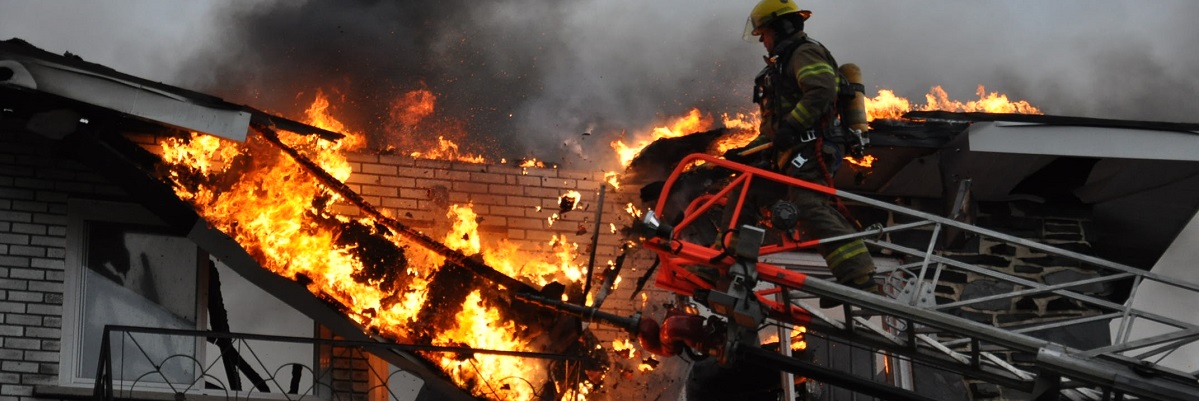 A firefighter on a ladder putting out a fire in a building