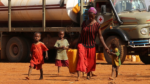 Mother with three kids walking with water container