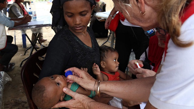 Mother holding infant while Red Cross worker assists