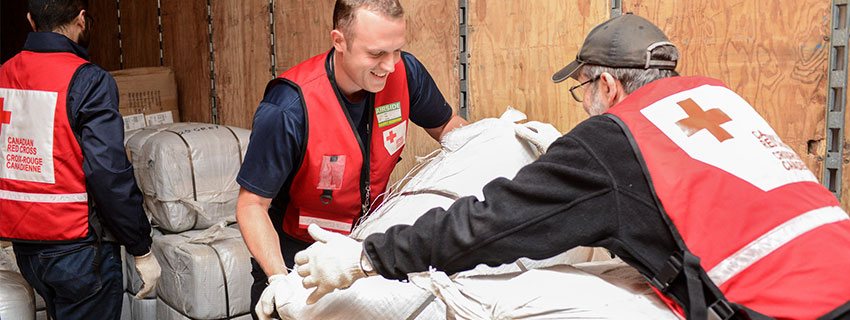 Three Red Cross volunteers pack a loading van with emergency supplies.